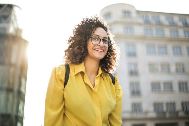 Portrait of a happy woman with curly hair and glasses smiling outdoors.