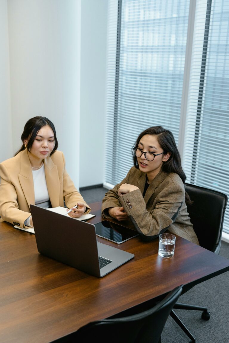 Two women in an office engaged in an online business meeting via laptop.
